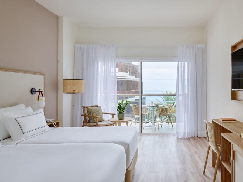 Moderne hotelkamer met twee tweepersoonsbedden en uitzicht op terras en zee