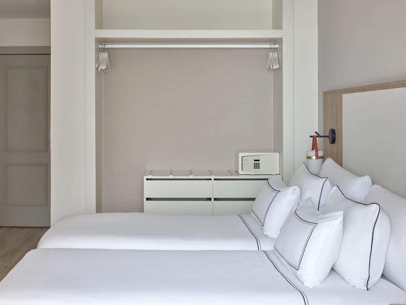 Minimalistische hotelkamer met twee bedden naast elkaar en een open kledingkast.