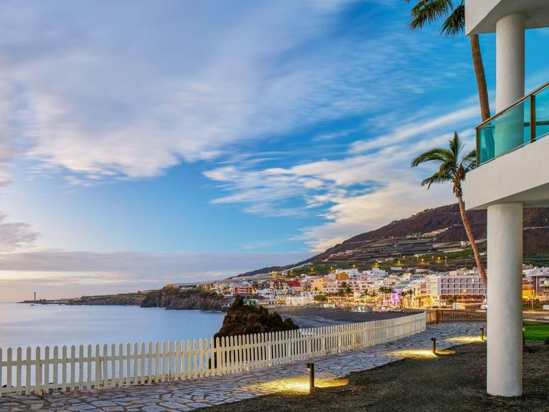 Uitzicht op een kuststad met zee, bergen en blauwe lucht bij zonsondergang.
