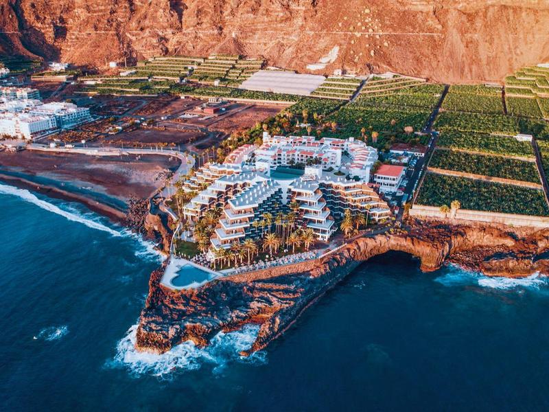 Luchtfoto van een hotel aan een rotsachtige kustlijn met de oceaan erbij bij zonsondergang.