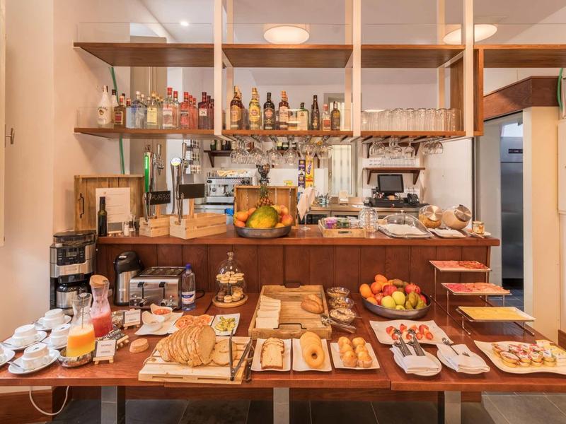 Auf einem Holztisch sind verschiedene Brotsorten, Obst und Frühstückszutaten in einer gemütlichen Küche arrangiert.