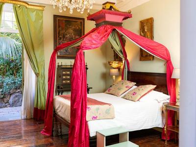 Elegant bedroom with four-poster bed and red drapes, green curtains on the window.