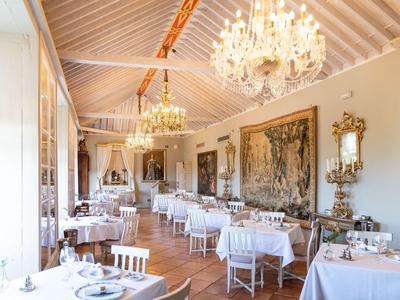 Elegant restaurant with white tablecloths, chandeliers, and tapestries in a bright room.
