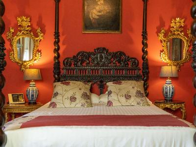 Elegantes Schlafzimmer mit roten Wänden, geschnitztem Bett und goldverzierten Spiegeln.