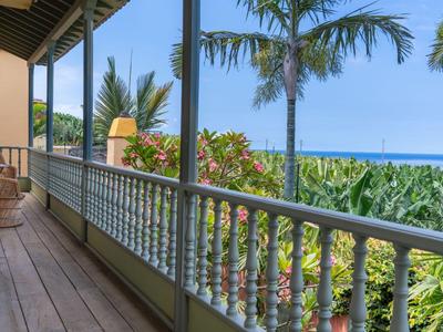 Balkon mit Holzgeländer und Blick auf Palmen und das Meer bei klarem Himmel.