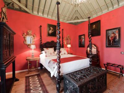 Ein Schlafzimmer mit roter Wand, Holzbett, antiken Möbeln und Gemälden an der Wand.