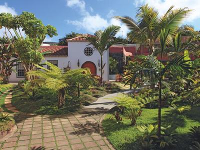 Ein tropischer Hotelgarten mit Palmen, Grünflächen und einem weißen Gebäude im Hintergrund.