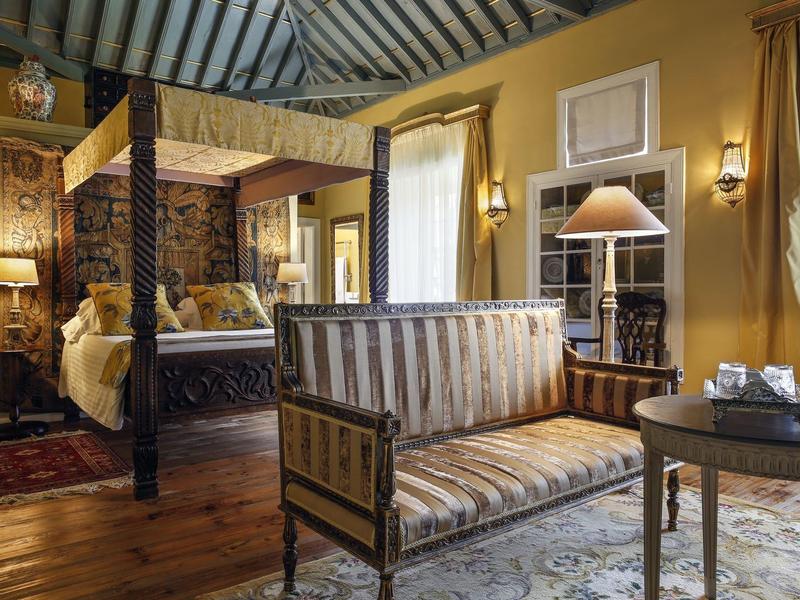 Cozy hotel room with four-poster bed, sofa, and elegant wooden furniture in warm colors.