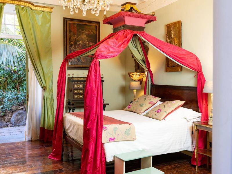 Elegant bedroom with four-poster bed and red drapes, green curtains on the window.