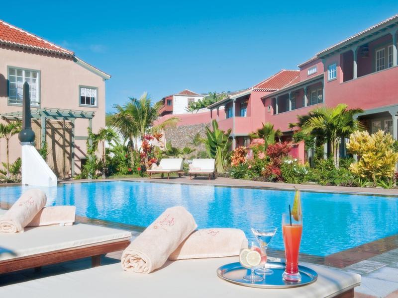 Hotel pool area with loungers, towels, and tropical plants on a sunny day