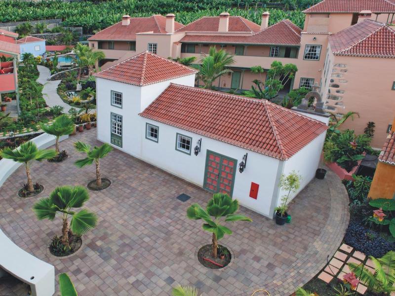 Aerial view of a small white holiday house with a red tiled roof and surrounding garden.