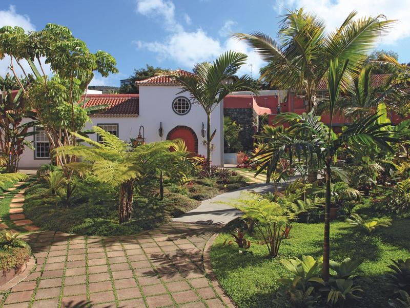 A tropical hotel with lush garden and palm trees under a sunny sky.