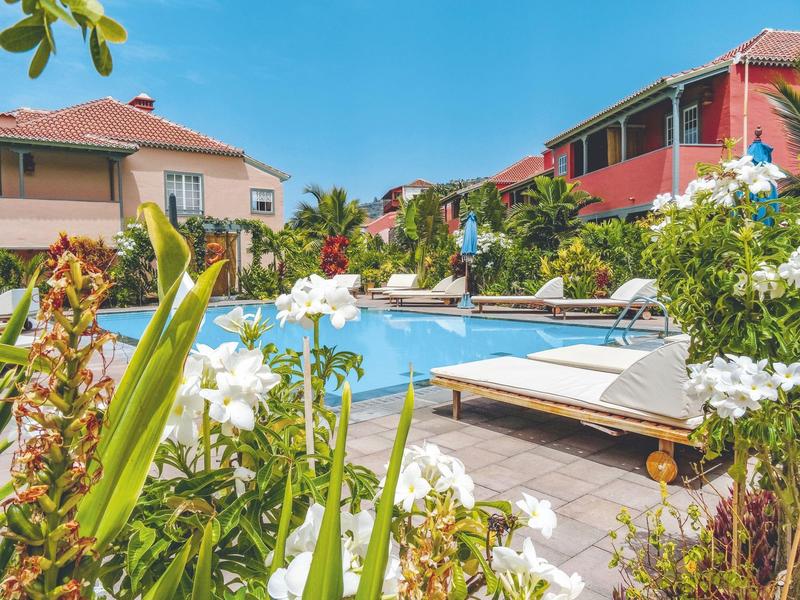 View of a pool area with lounge chairs and blooming plants in a hotel complex.