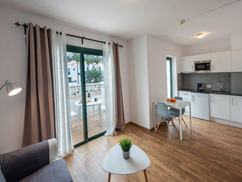 Sala luminosa con suelo de madera, mesa pequeña, sofá y acceso a balcón con vista exterior.