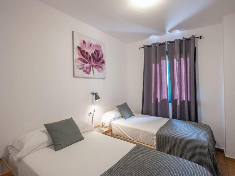 Habitación de hotel sencilla con dos camas individuales, cortinas grises y pared blanca con decoración floral.