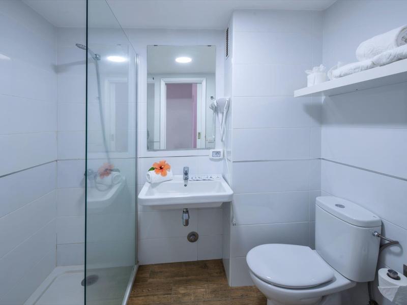 Baño moderno de hotel con inodoro, lavabo, espejo y ducha a ras de suelo con mampara de cristal.