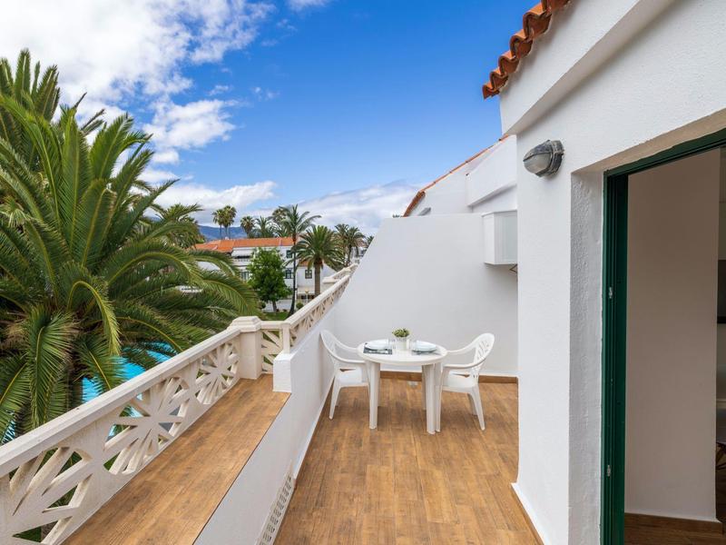 Balcón con mesas y sillas blancas junto a palmeras y cielo azul en un hotel.
