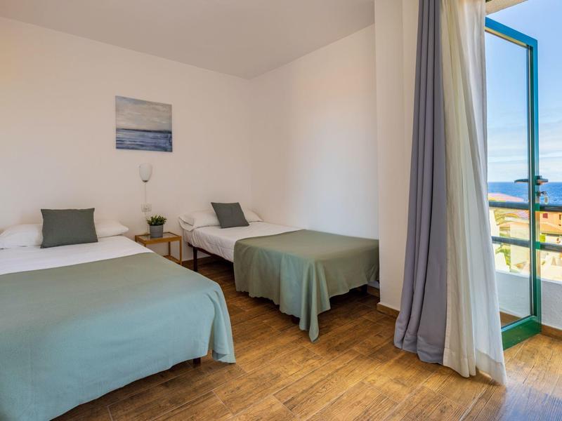 Habitación de hotel luminosa con dos camas individuales, suelo de madera y balcón con vista al mar.