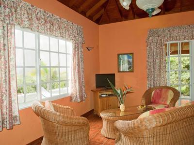 Gemütliches Wohnzimmer mit Korbmöbeln, großem Fenster und oranger Wandfarbe.