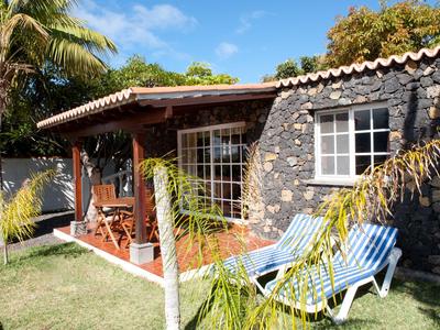 Gemütliches Ferienhaus mit Terrasse, zwei Liegestühlen und tropischem Garten