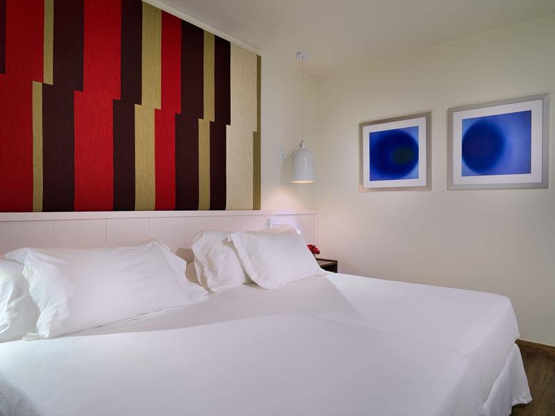 Habitación de hotel moderna con cama grande, ropa de cama blanca y decoración de pared.