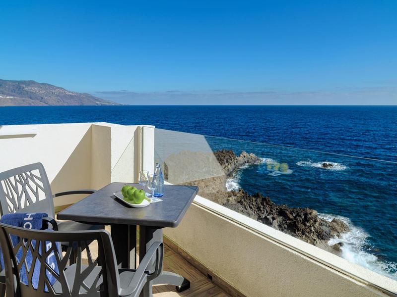 Balcón con mesa y sillas con vista al mar y al cielo azul claro.
