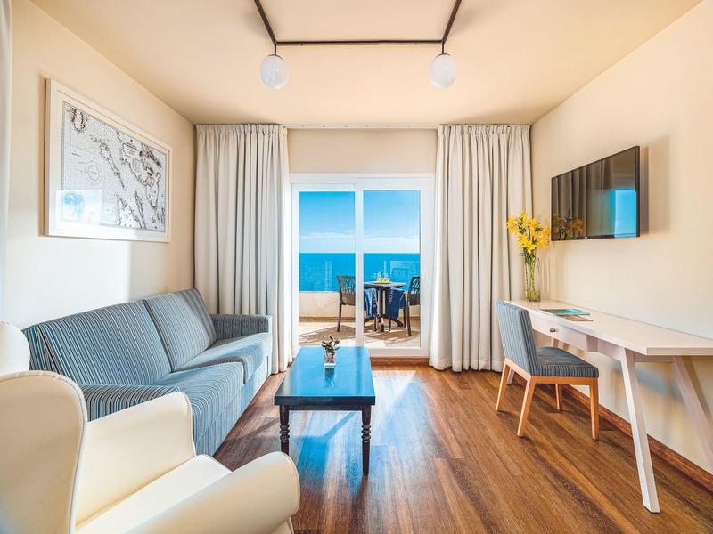 Sala luminosa con vista al mar, sofá, mesa y televisor en apartamento vacacional moderno.