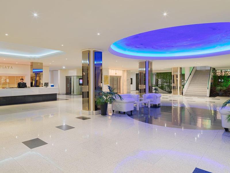 Vestíbulo de hotel iluminado, con área de descanso y mostrador de recepción moderno.