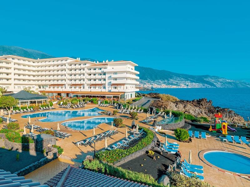 Gran hotel junto al mar con varias piscinas y áreas verdes bajo un cielo azul despejado.