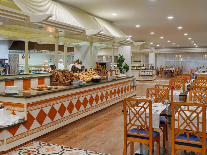 Área de buffet con sillas y mesas de madera en un restaurante luminoso.