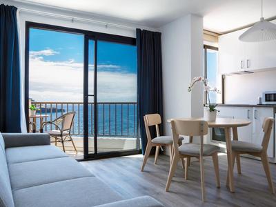 Helles Hotelzimmer mit Balkon, Sofa, Esstisch, Stühlen und Meerblick.