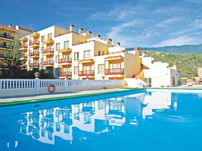 Hotel with outdoor pool, surrounded by multi-story buildings and mountains in the background.