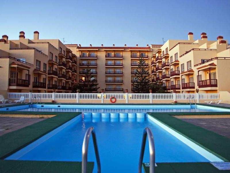 A large outdoor pool in front of a multi-story hotel building under a clear sky.