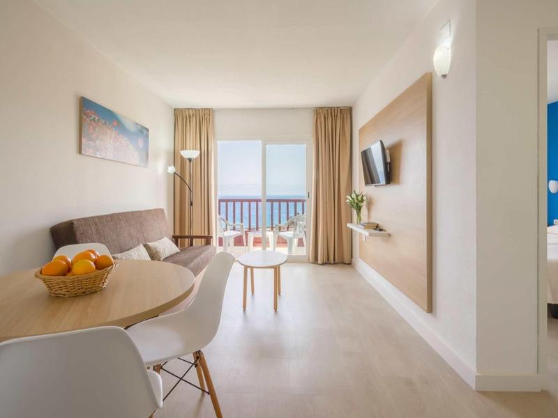 Bright hotel room with dining table, living area, and balcony with sea view