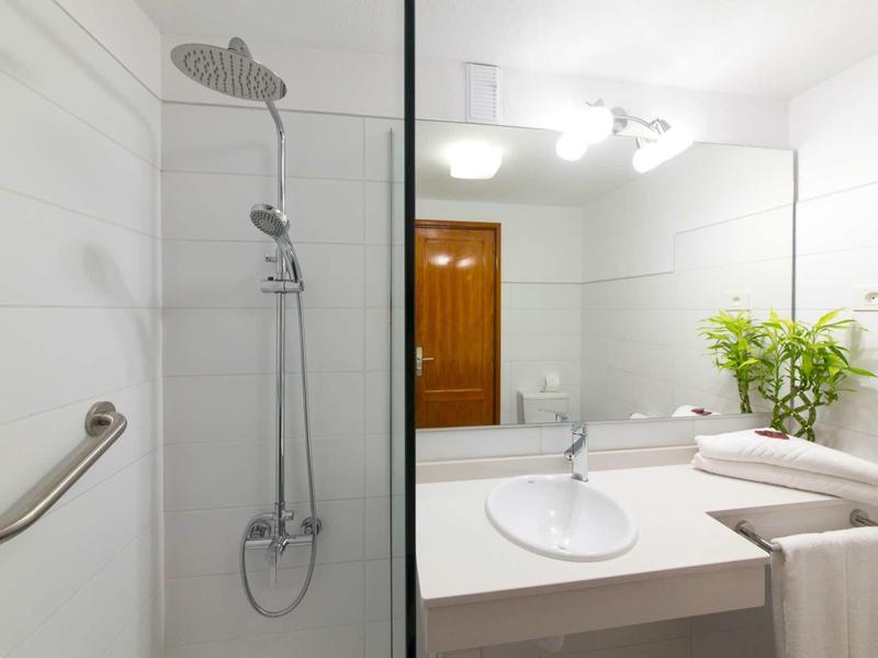 Bright bathroom with shower, sink, mirror, and fresh plant.