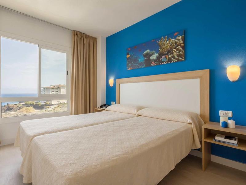 Hotel room with two single beds, blue wall, and window overlooking the sea.