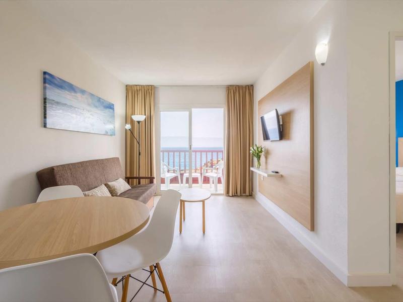 Bright hotel room with dining table, balcony, and sea view.