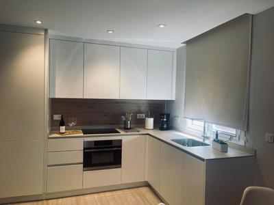 Moderne Hotelküche mit weißen Schränken, Backofen, Kaffeemaschine und grauen Jalousien.