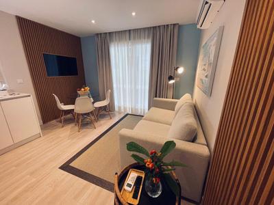 Moderner Hotelzimmer mit Sitzbereich, Esstisch und Balkon mit Vorhängen.
