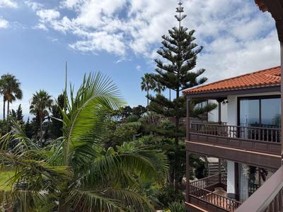 Hotel z balkonem i tropikalnymi palmami na tle niebieskiego nieba z chmurami.