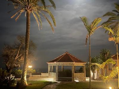 Nocna scena hotelowa z oświetloną ścieżką, palmami i jasnym księżycem na pochmurnym niebie.