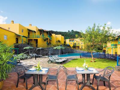 Yellow vacation homes surround a pool with tables and chairs on a terrace.