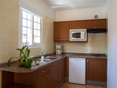 Cocina pequeña con muebles de madera, microondas, cafetera, minibar y ventana con luz natural.