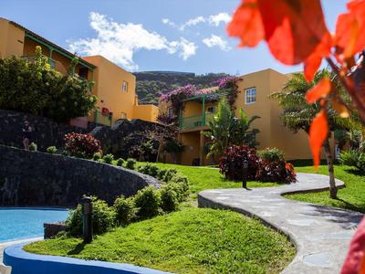 Path with well-kept lawn and colorful flowers in a resort with yellow buildings and mountains in the background.