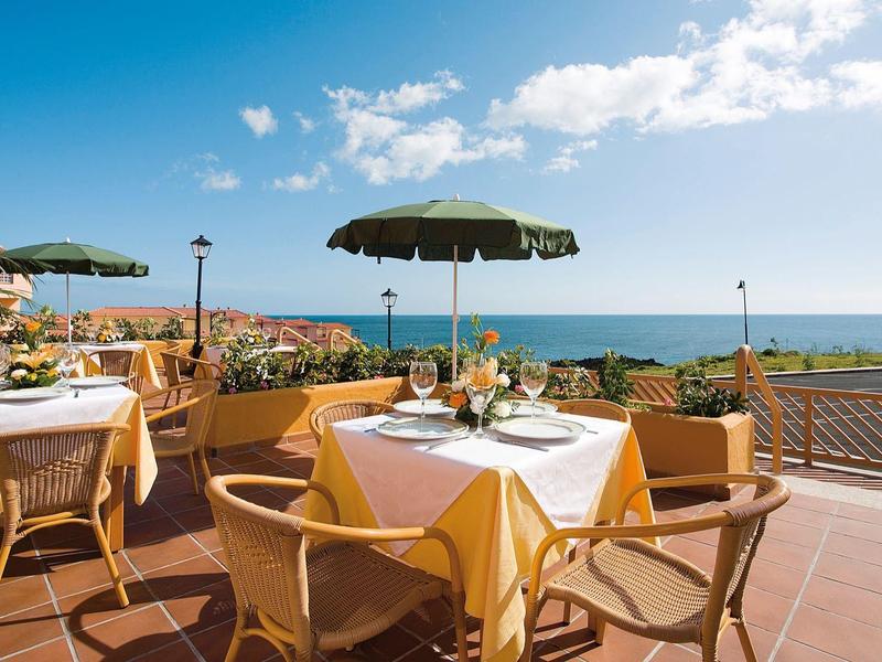 Terraza con mesas puestas, sombrillas y vista al mar bajo un cielo despejado.
