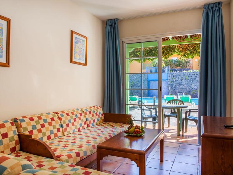 Área de estar acogedora con sofá estampado, mesa de madera y vista a terraza con mesa y sillas.