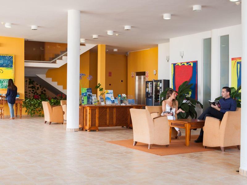 Habitación con paredes claras, sillones cómodos y mesa de libros en un área de descanso del hotel.