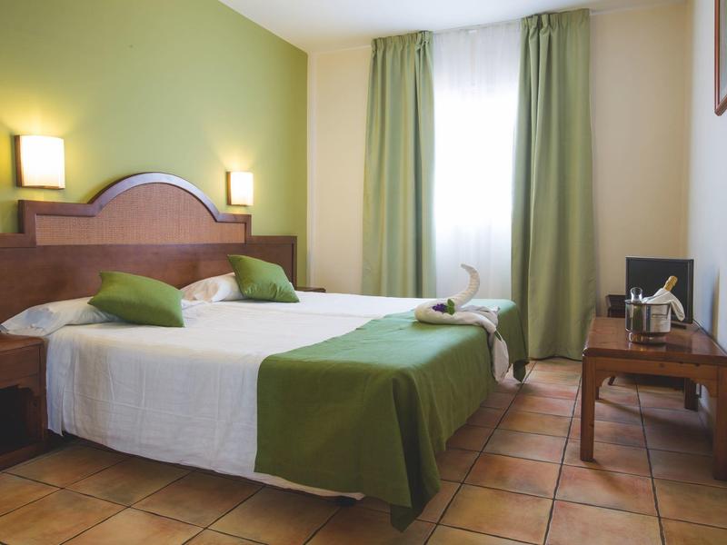 Habitación de hotel acogedora con cama doble, acentos verdes y luz natural brillante.