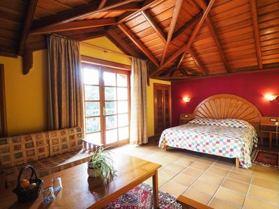 Acogedor dormitorio con techo de vigas de madera, cama grande y área de estar junto a puerta a terraza.