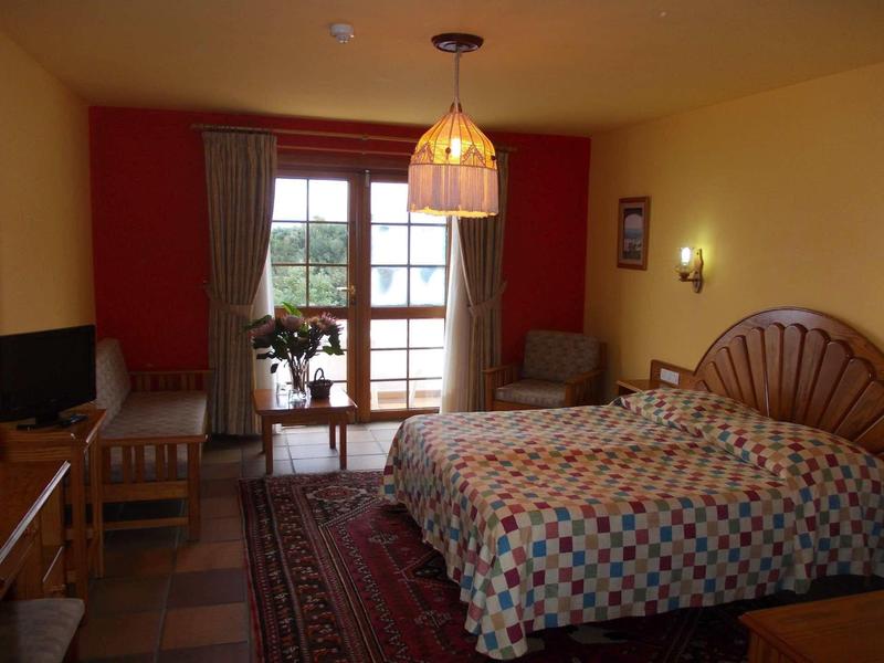 Habitación de hotel acogedora con cama doble, ventana grande y zona de estar con silla y mesa.